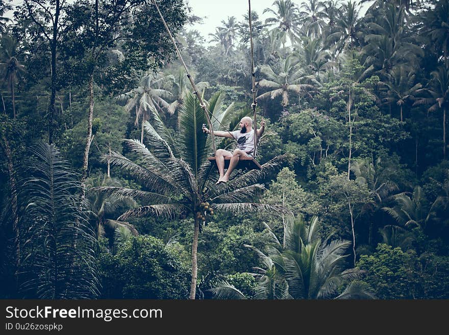 BALI, INDONESIA - DECEMBER 26, 2017: Man having fun on the swing in the jungle of Bali island. Rainforest, swing. BALI, INDONESIA - DECEMBER 26, 2017: Man having fun on the swing in the jungle of Bali island. Rainforest, swing.