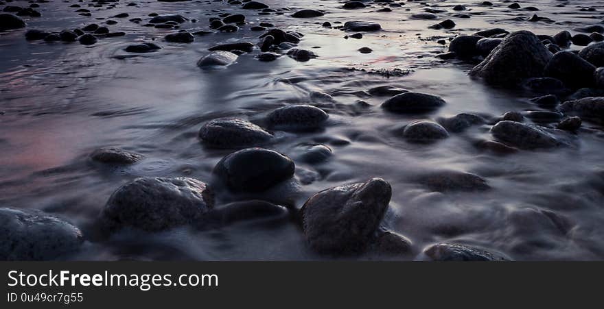 Water washes over pebbles along the coast in a long exposure shot of the tauranga harbour