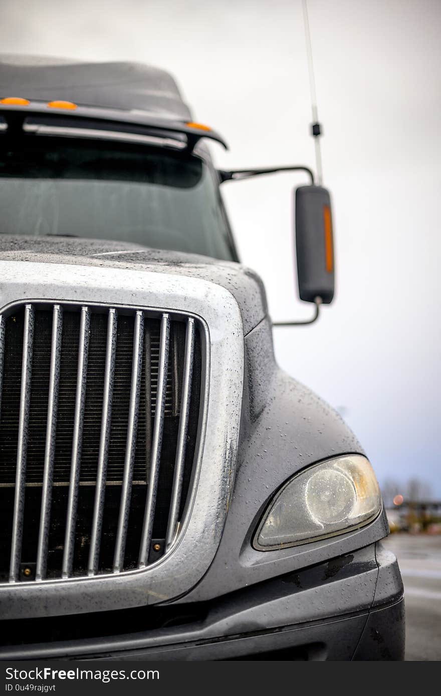 Front of dark gray big rig semi truck with efficient eco-friendly diesel engine and chrome grille with rain drops standing on the industrial parking lot. Front of dark gray big rig semi truck with efficient eco-friendly diesel engine and chrome grille with rain drops standing on the industrial parking lot.