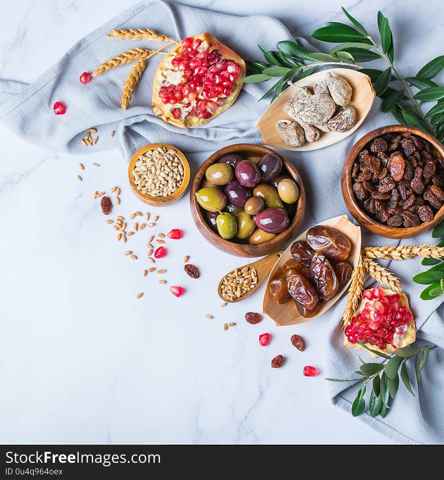 Symbols of judaic holiday Tu Bishvat, Rosh Hashana new year of the trees. Mix of dried fruits, date, fig, grape, barley, wheat, olive, pomegranate on a marble table. Copy space background. Symbols of judaic holiday Tu Bishvat, Rosh Hashana new year of the trees. Mix of dried fruits, date, fig, grape, barley, wheat, olive, pomegranate on a marble table. Copy space background