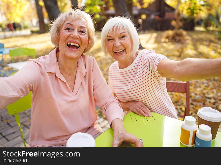 Beautiful old women laughing sitting in the park cafe together on the autumn day. Beautiful old women laughing sitting in the park cafe together on the autumn day