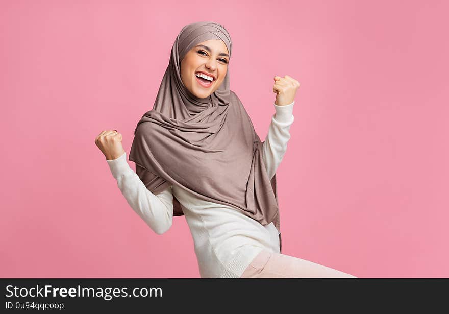 Yes. Happy muslim woman in hijab rejoicing success, raising hands and exclaiming with winner face expression. Yes. Happy muslim woman in hijab rejoicing success, raising hands and exclaiming with winner face expression