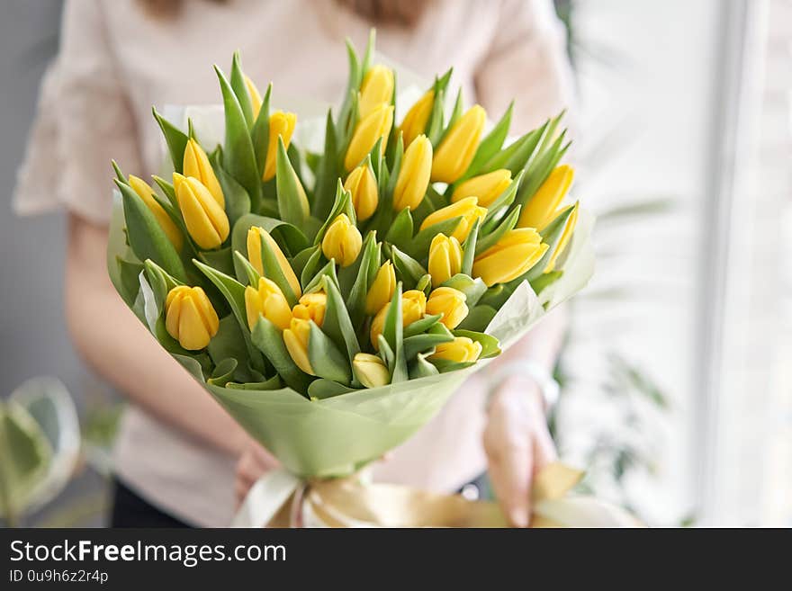 Young beautiful woman holding a spring bouquet of yellow tulips in her hand. Bunch of fresh cut spring flowers in female