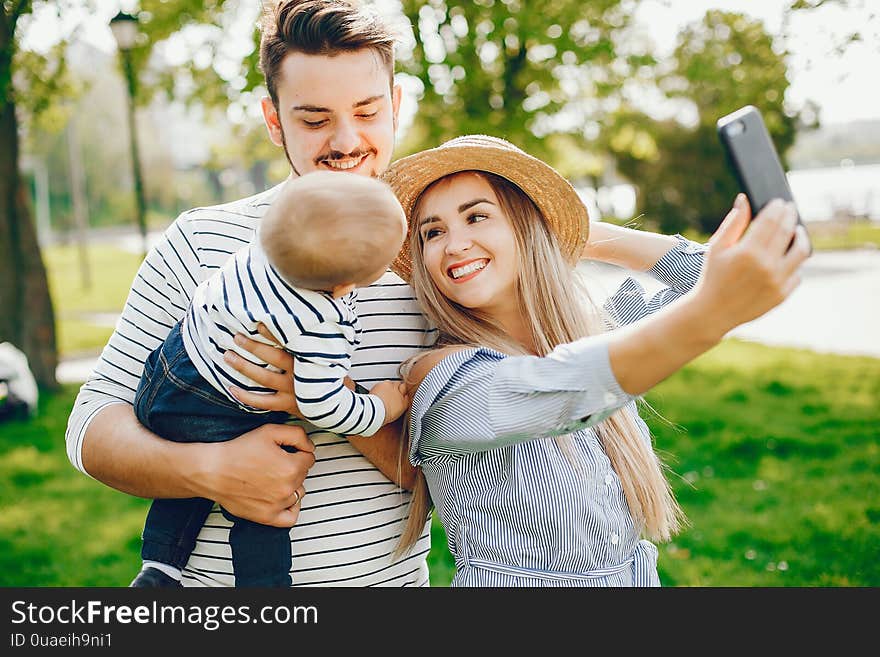 A young and beautiful blonde mother in a blue dress, along with her handsome men dressed in a white jacket, playing with her little son in the summer solar park. A young and beautiful blonde mother in a blue dress, along with her handsome men dressed in a white jacket, playing with her little son in the summer solar park