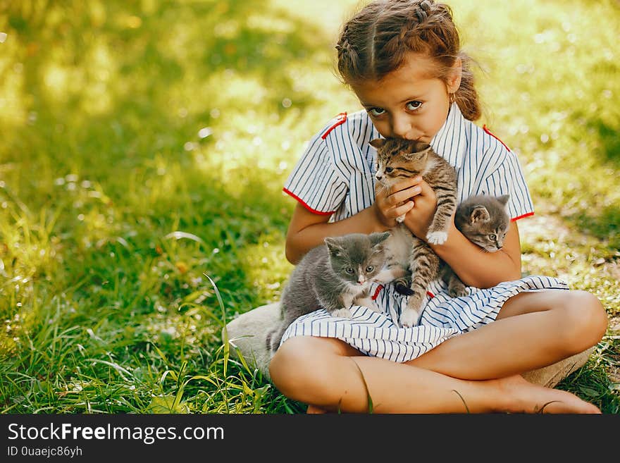 Beautiful and cute girl in blue dresses with beautiful hairstyles and make-up sitting in a sunny green garden and playing with a cats. Beautiful and cute girl in blue dresses with beautiful hairstyles and make-up sitting in a sunny green garden and playing with a cats