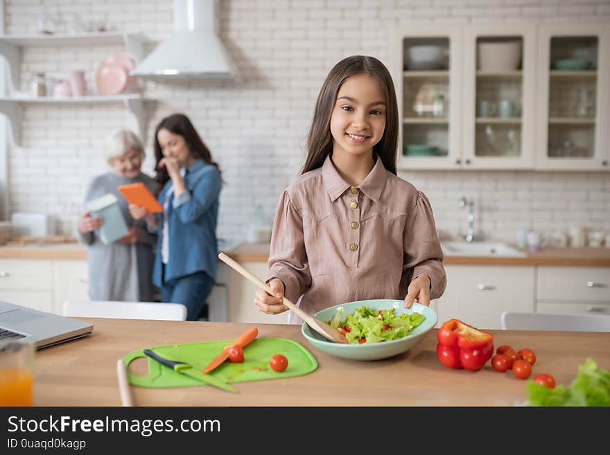 Little girl in the kitchen showing cooked salad.