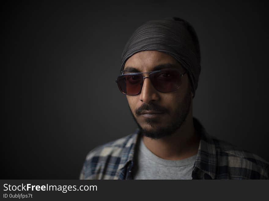 Indian Bengali handsome beard macho guy/man/male in cowboy hat and sun glass holding a tobacco pipe  on his mouth in front of a grey copy space studio background. Copy space facial expressions. Indian Bengali handsome beard macho guy/man/male in cowboy hat and sun glass holding a tobacco pipe  on his mouth in front of a grey copy space studio background. Copy space facial expressions