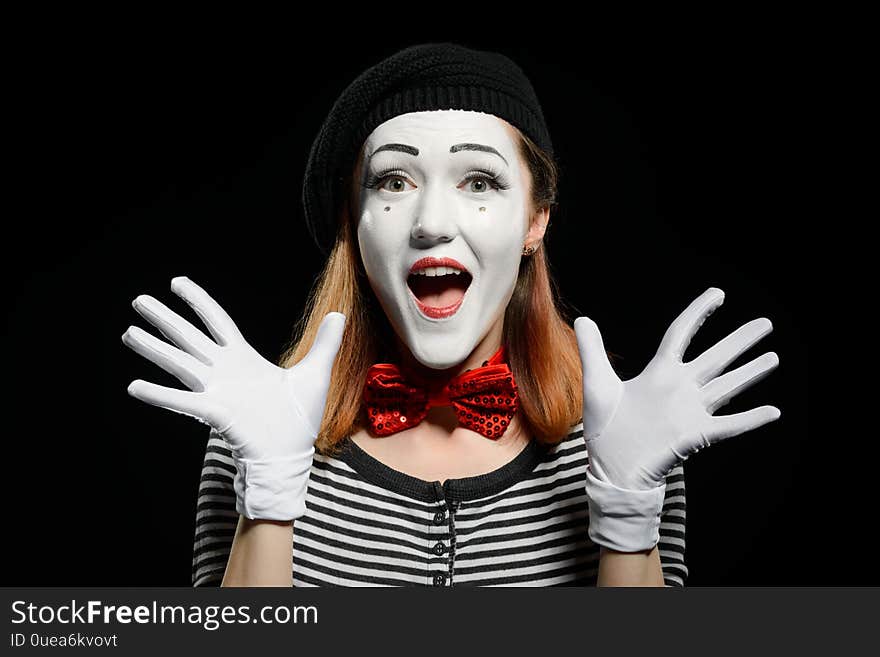 Happy female mime on black background. Cute actress is using exaggerated face expressions, hand gestures and no words in acting a pantomime.