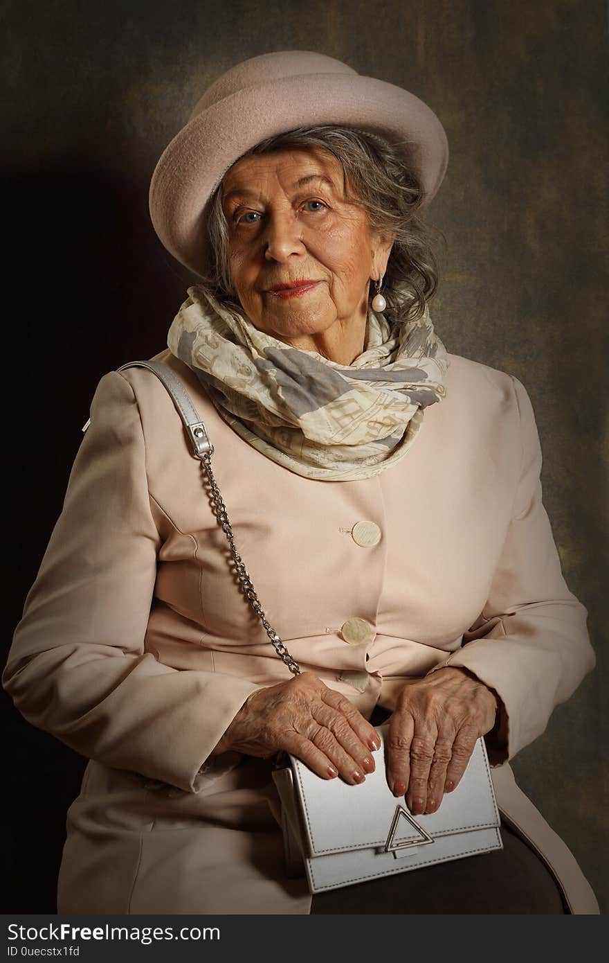 Portrait of an old woman in a hat, scarf and handbag on a brown background