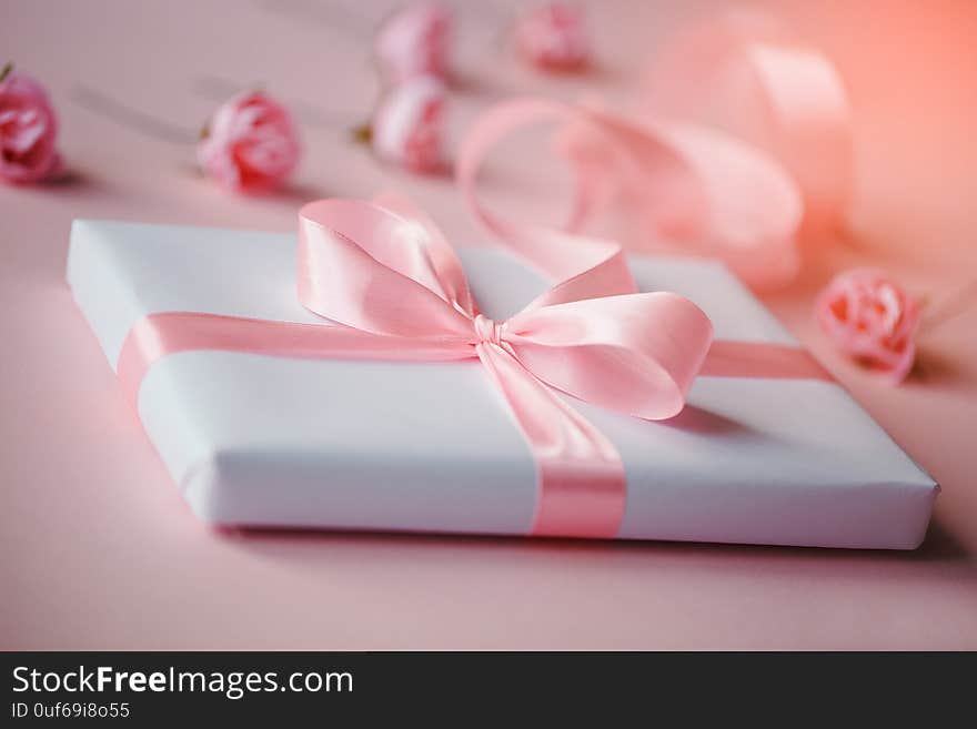 Composition of a white box and small pink flowers on a light pink background. Packing of gifts