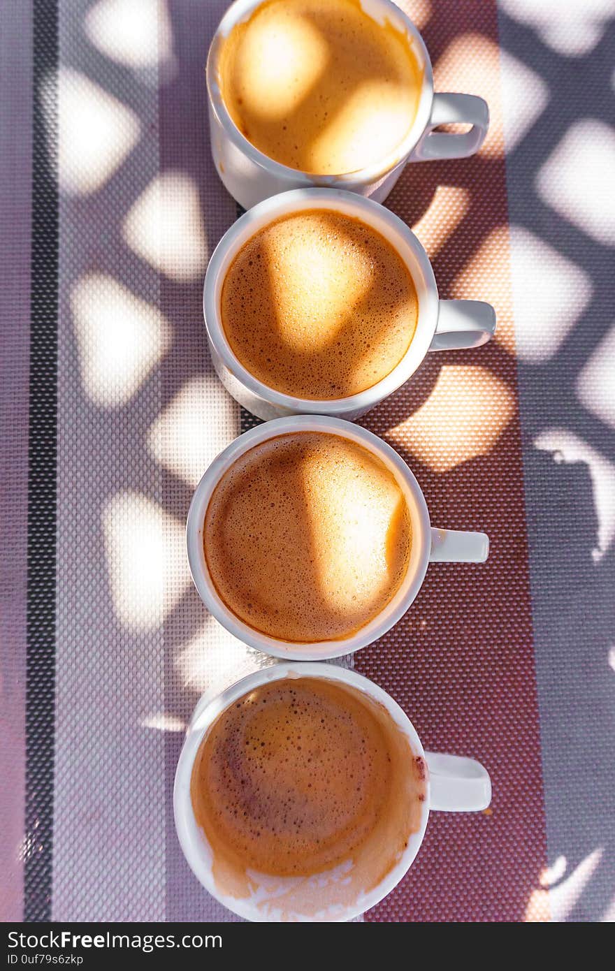 Four cups of coffee on the table illuminated by the sun through the lattice roof top view. Four cups of coffee on the table illuminated by the sun through the lattice roof top view