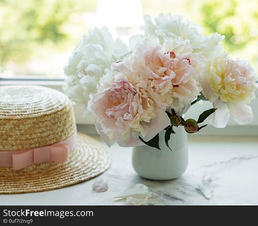 Straw hat on a table with peony flowers in vase at the window. Straw hat on a table with peony flowers in vase at the window