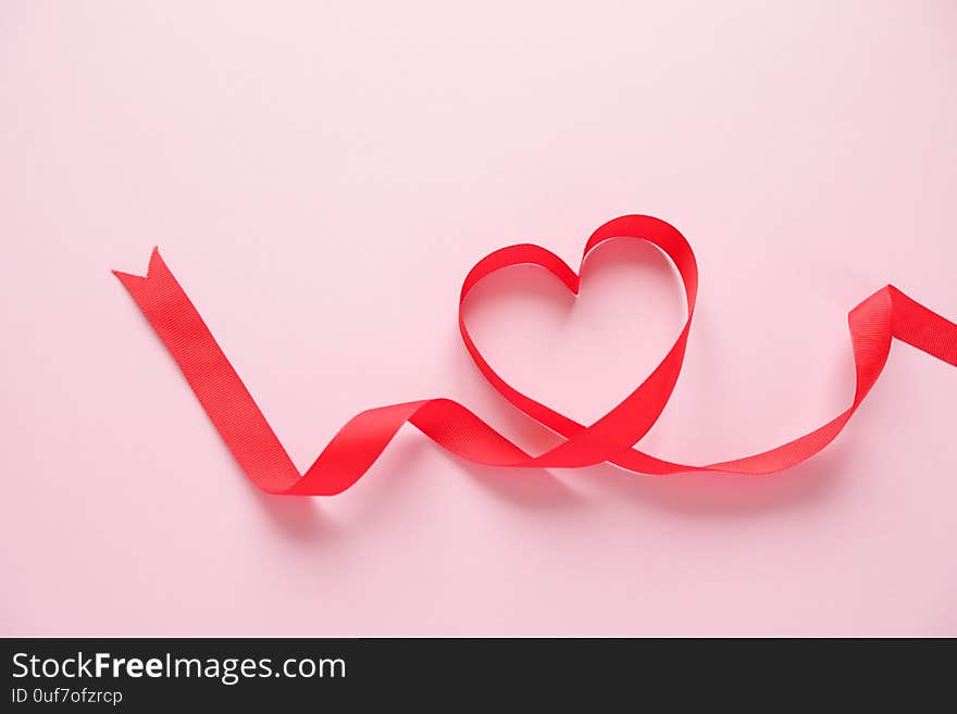 Red ribbon in the shape of a heart on a pink background