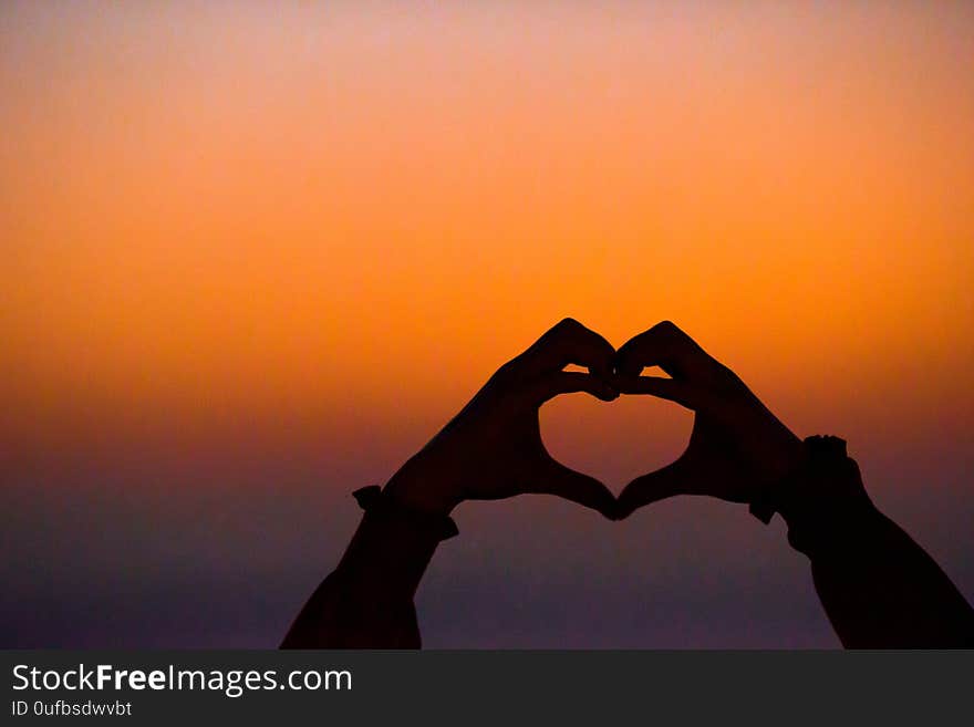 Silhouette of heart made by kids hand at sunset