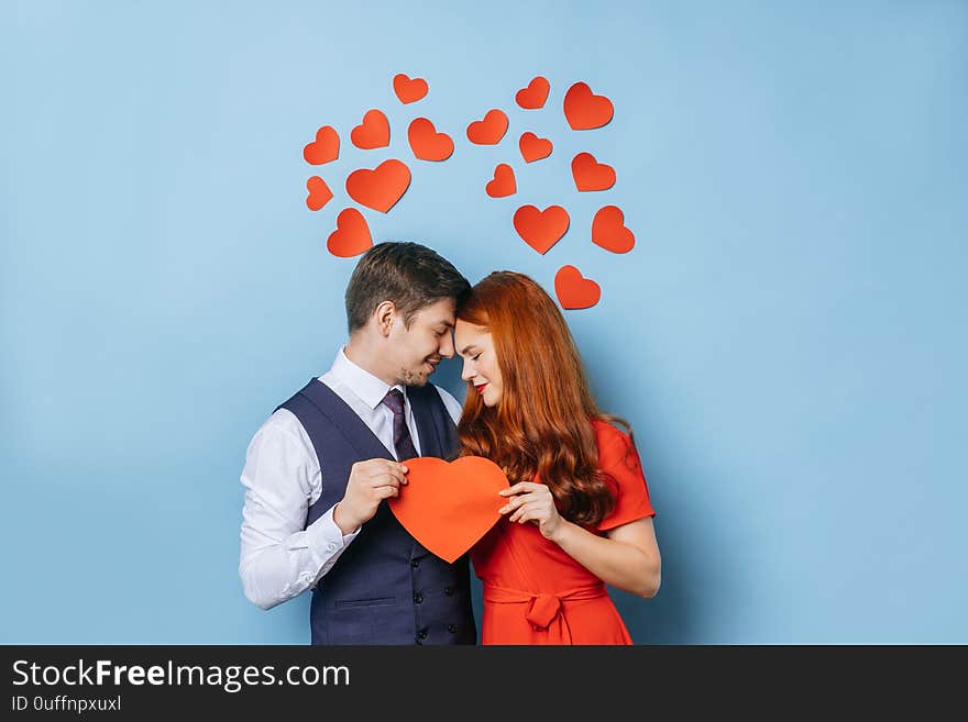 Portrait of cute caucasian couple holding heart made from cardboard, stand next to each other and feel tenderness. isolated blue background. love concept. Portrait of cute caucasian couple holding heart made from cardboard, stand next to each other and feel tenderness. isolated blue background. love concept