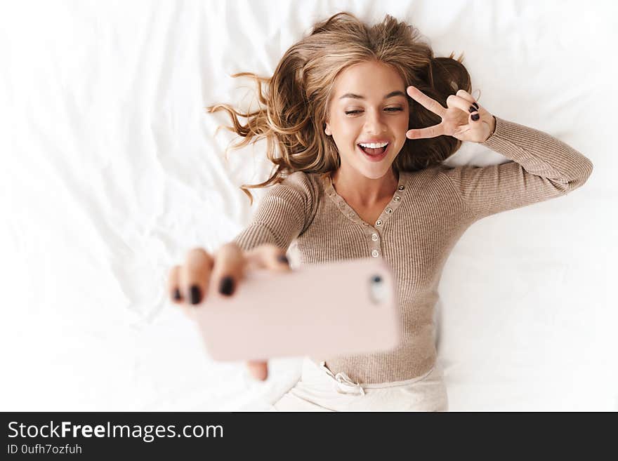 Photo of young smiling woman taking selfie and gesturing peace sign