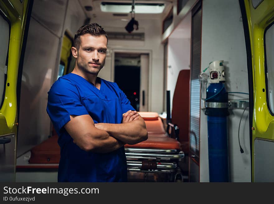 Young paramedic in medical uniform look at camera and smile, ambulance car on the background. Young paramedic in medical uniform look at camera and smile, ambulance car on the background