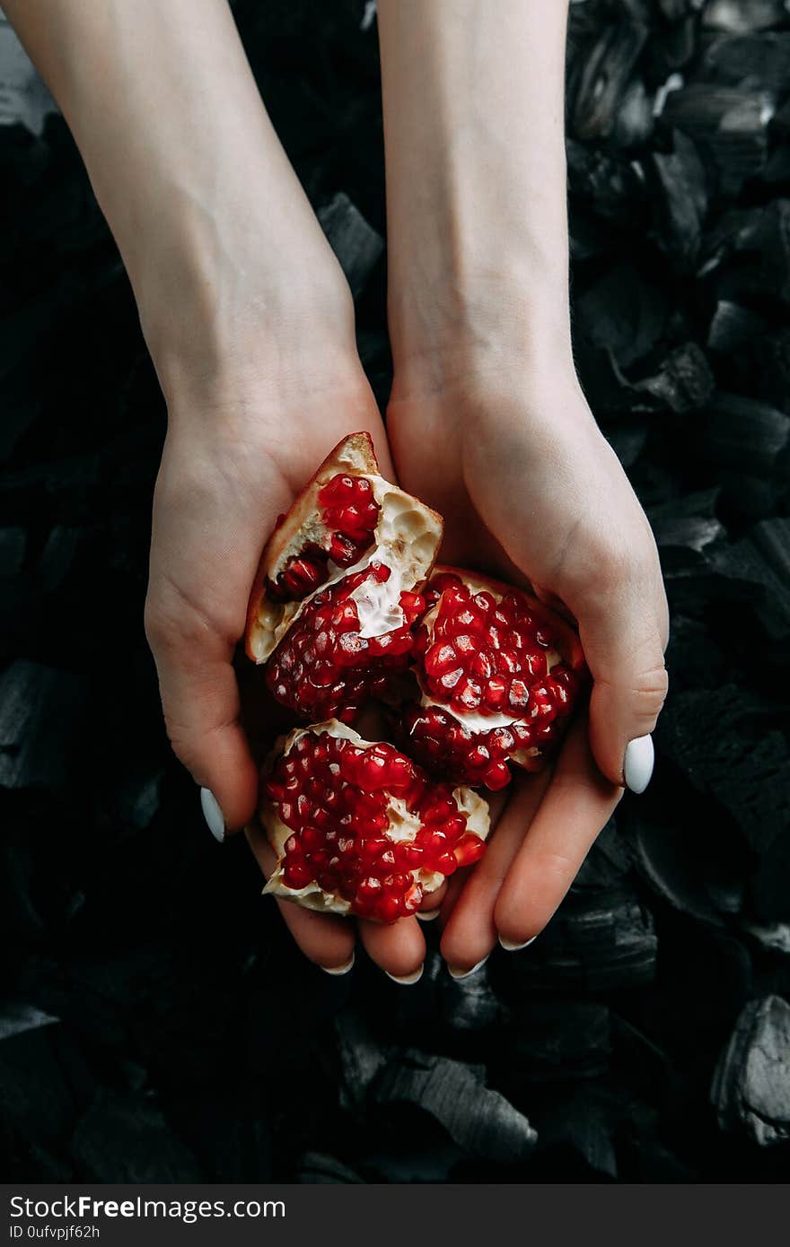 Broken pomegranate slices on a dark texture. Preparation for hookah. Ripe garnet in the hands of a girl. Black charcoal background