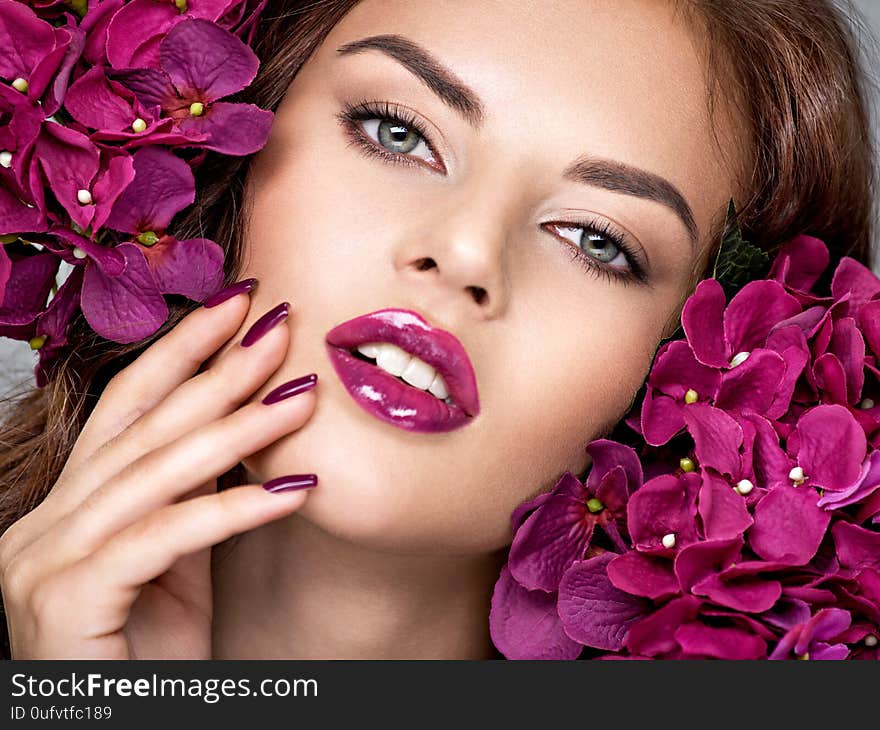 Beautiful  woman with purple make-up of lips and fingernails. Closeup woman`s portrait with flowers. Young caucasian gorgeous attractive girl. Model. Vivid make-up. Sexy female. Violet fingernails