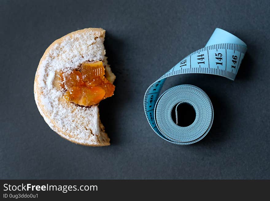 A piece of cake and a centimeter on a black background. The concept of losing weight, abstinence from sweets. Bitten cake on the board. Time to go on a diet and losing weight