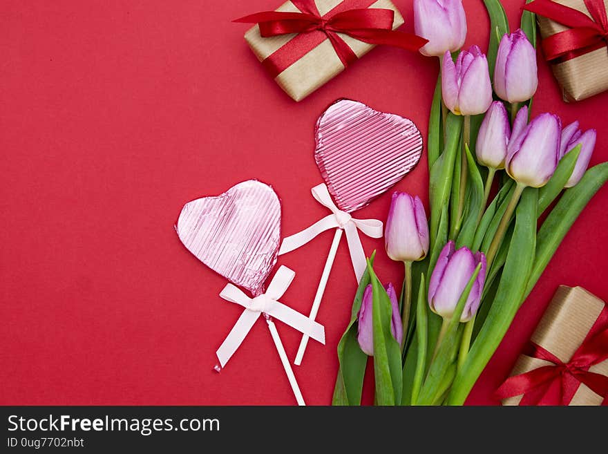 Pink or purple tulip flowers heart shaped chocolate and gift boxes on red background. Top view with copy space.