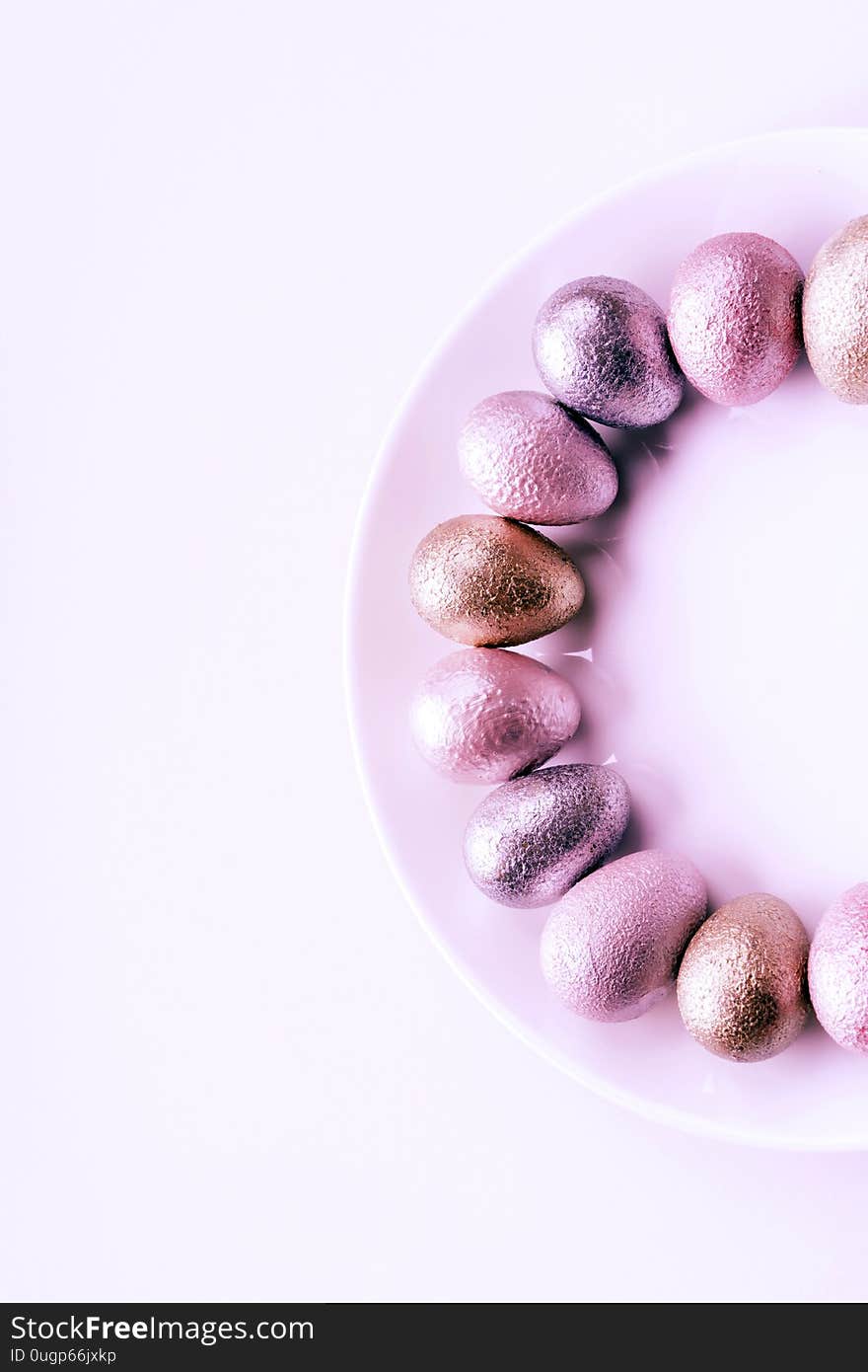 Colored painted pearl chicken and quail eggs of pink, silver, golden color on a purple plate pastel background. Minimalistic creative idea easter festive flat lay. Copyspace for text. Colored painted pearl chicken and quail eggs of pink, silver, golden color on a purple plate pastel background. Minimalistic creative idea easter festive flat lay. Copyspace for text