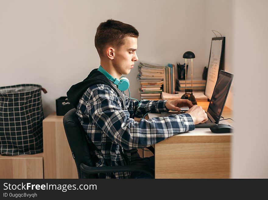 Teenage boy doing homework using computer sitting by desk in room alone. Teenager warching video and browsing internet on personal laptop