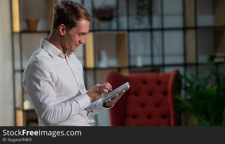 Use of applications and modern technologies for work and communication. Portrait of a positive and confident young man in a classic white shirt. Happy guy student with the tablet