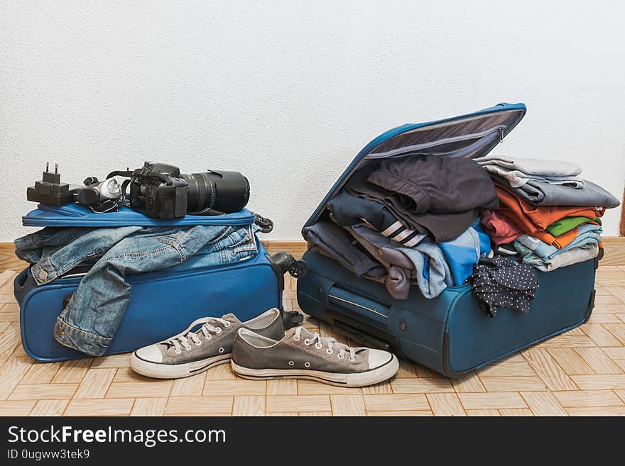 Open blue suitcase with a lot of clothing, impossible to close, preparing for vacations, white background. Open blue suitcase with a lot of clothing, impossible to close, preparing for vacations, white background