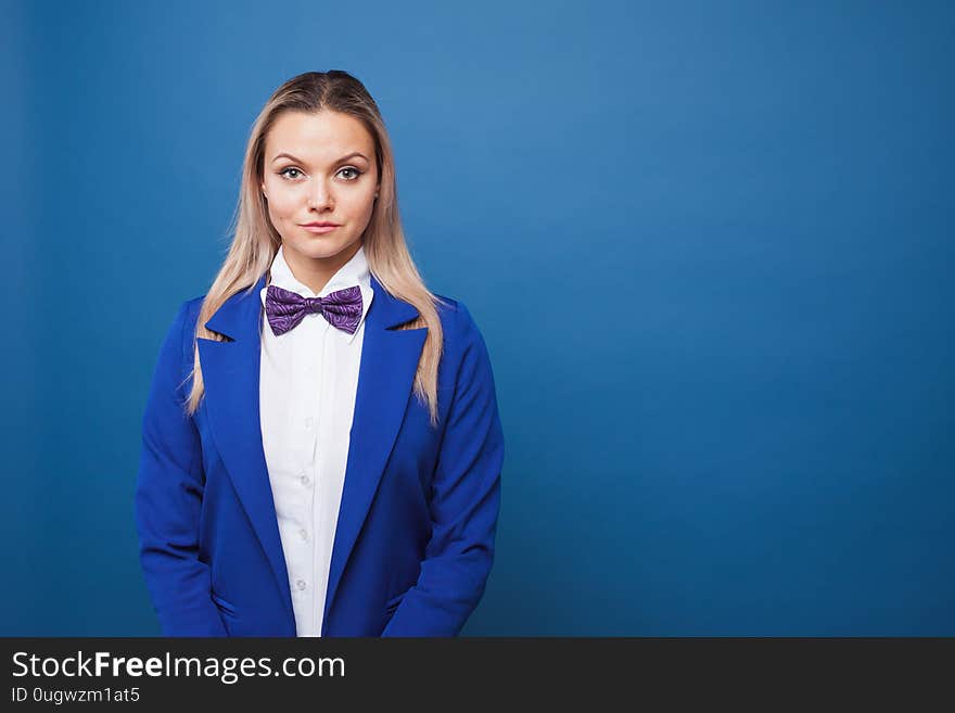 Cute girl in blue jacket with bow tie on blue background. Funny business portrait, copy space