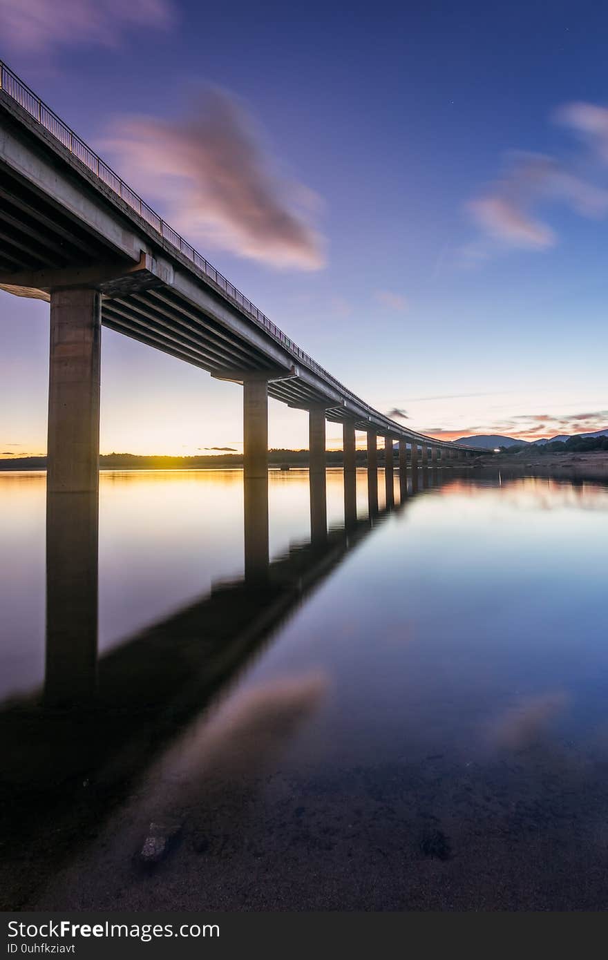 Crossing the water thru the highway. Highway bridge is crossing the Valmayor Lake in Madrid. Sunset, some clouds and light trails