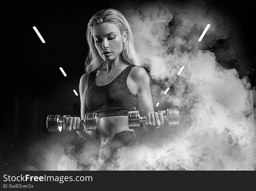 Charming sportswoman posing in the gym with dumbbells. The concept of bodybuilding, fitness, stretching, healthy eating. Mixed media