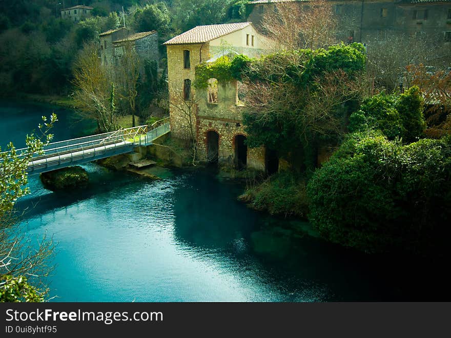 Ancient mill ruin on a turquoise colored river influenced by limestone in an Italian valley with climbing vegetation. Ancient mill ruin on a turquoise colored river influenced by limestone in an Italian valley with climbing vegetation