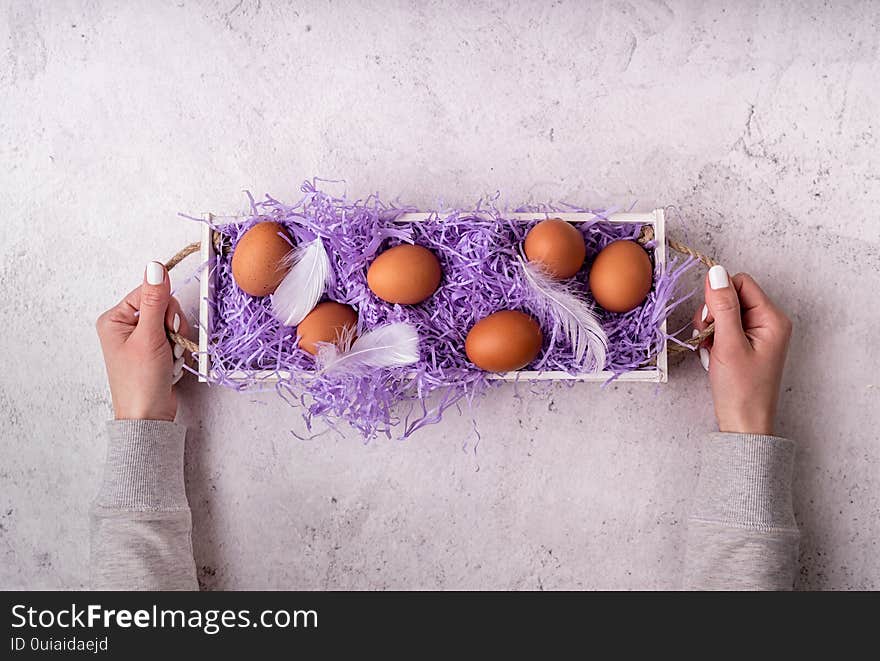 Easter holiday concept. Woman hands holding white wooden box with chicken eggs on white marble background top view flat lay