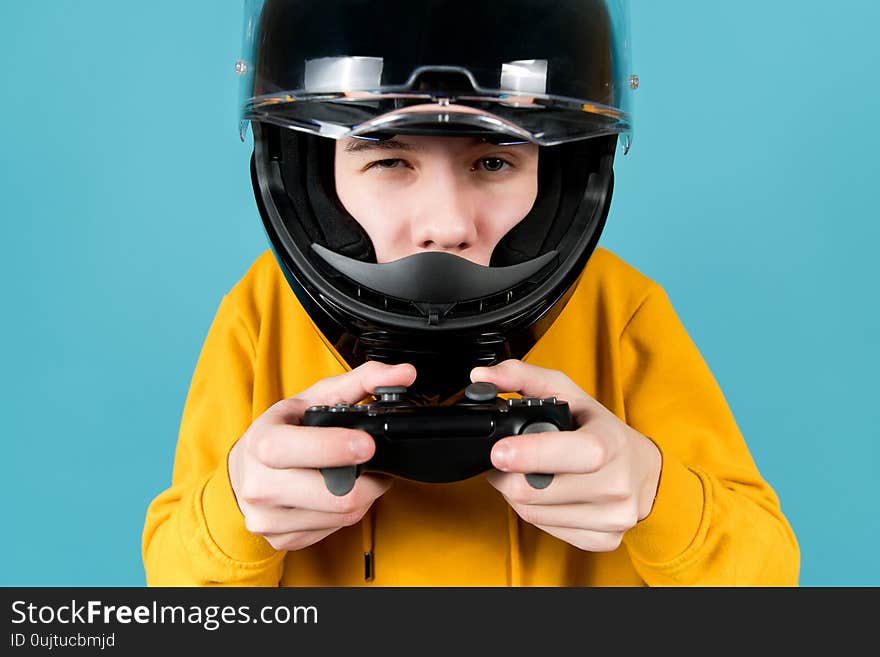 Close-up of a teenager in a black helmet and with a black joystick in his hands on a blue background. Close-up of a teenager in a black helmet and with a black joystick in his hands on a blue background