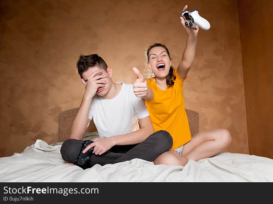 The teenager is upset that he lost a computer game to his sister, covers his face with his palm. In their hands they hold modified joysticks without identification marks