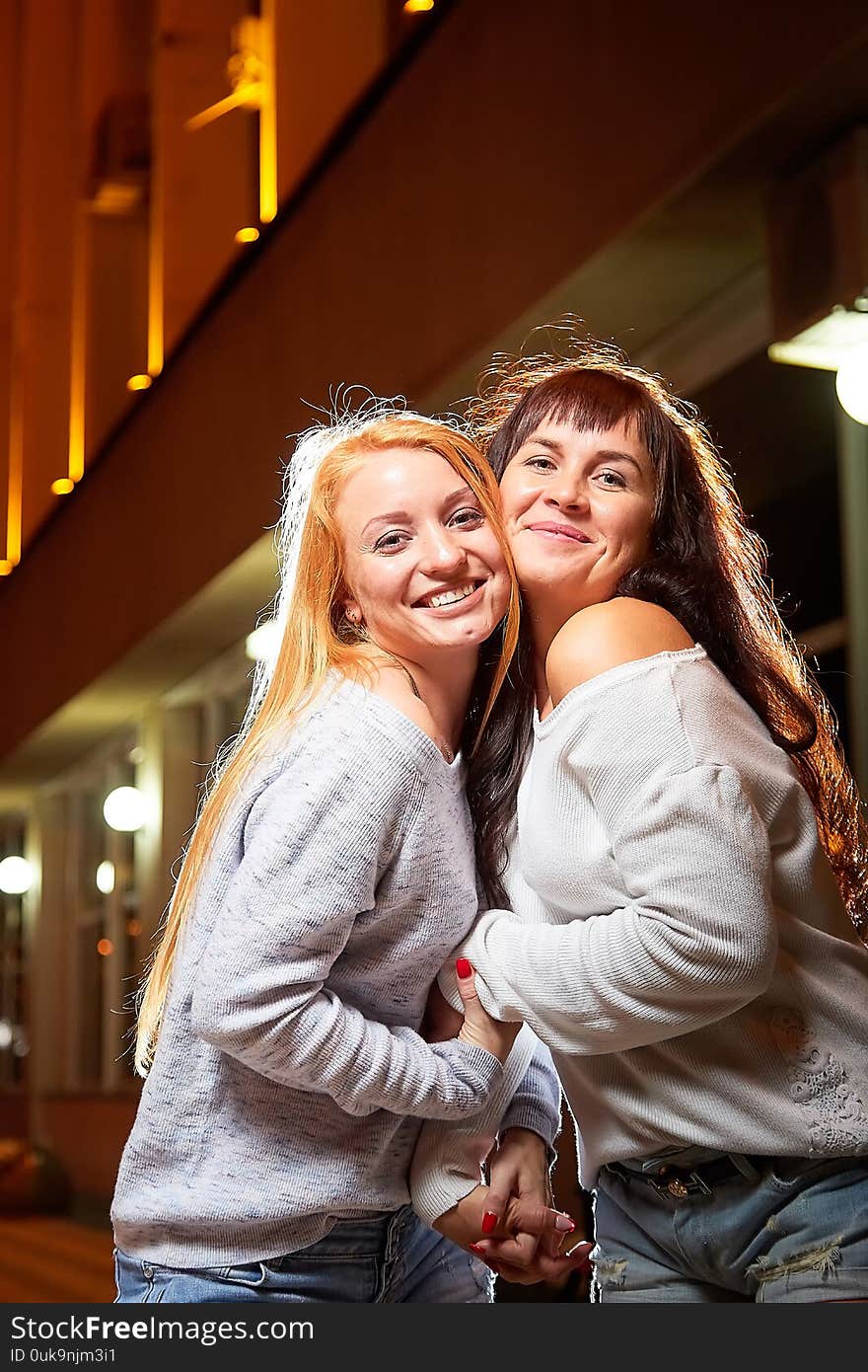 Two female friends on a city street at night. Girls and black background with light outdoors