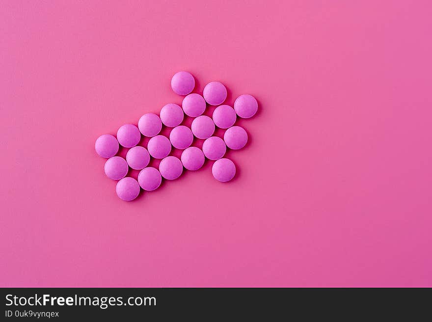 Close-up of pink pills lie on a pink surface depicting an arrow to the right side. Place for advertising. Problem Solving Concept