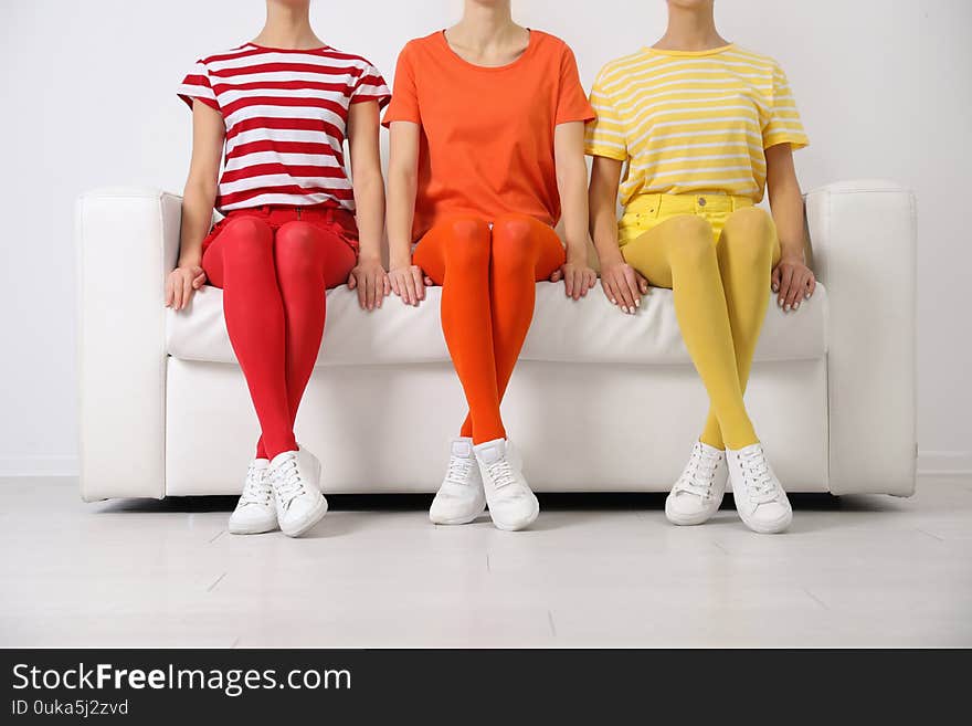 Women wearing bright tights sitting on sofa indoors, closeup