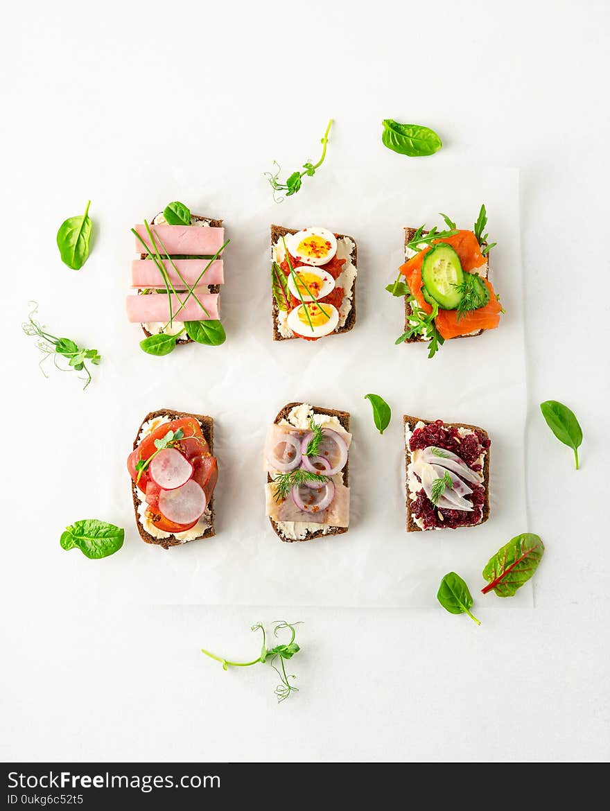 Selection of Danish smorrebrod open sandwiches, green salad leaves on parchment paper on white background. Top view, portrait orientation