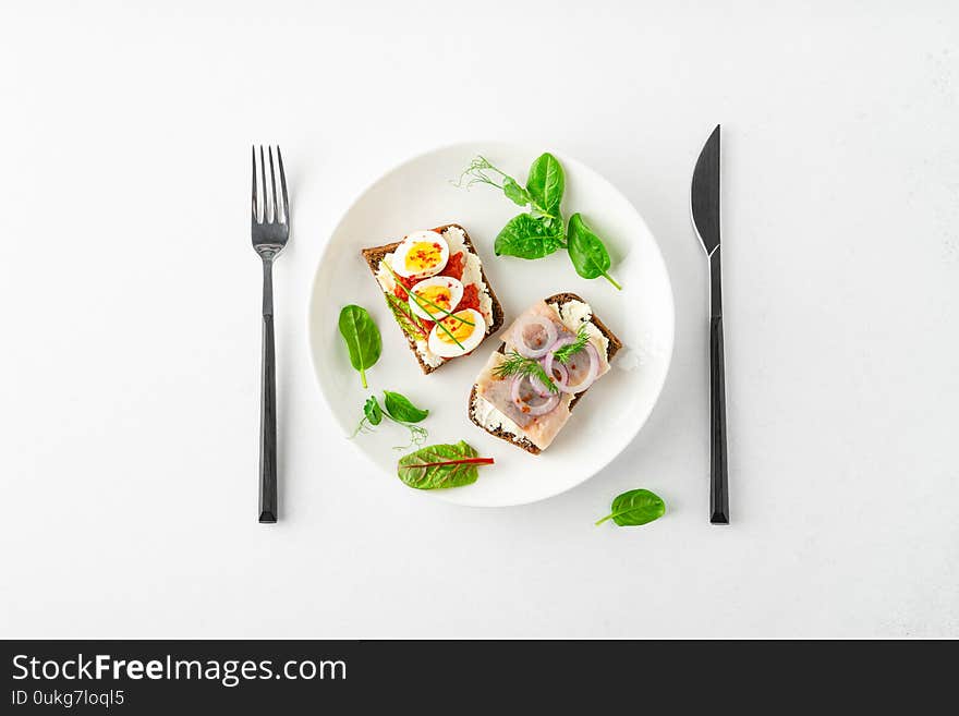 Danish smorrebrod open sandwiches on white plate, fork and knife, green salad leaves on white background