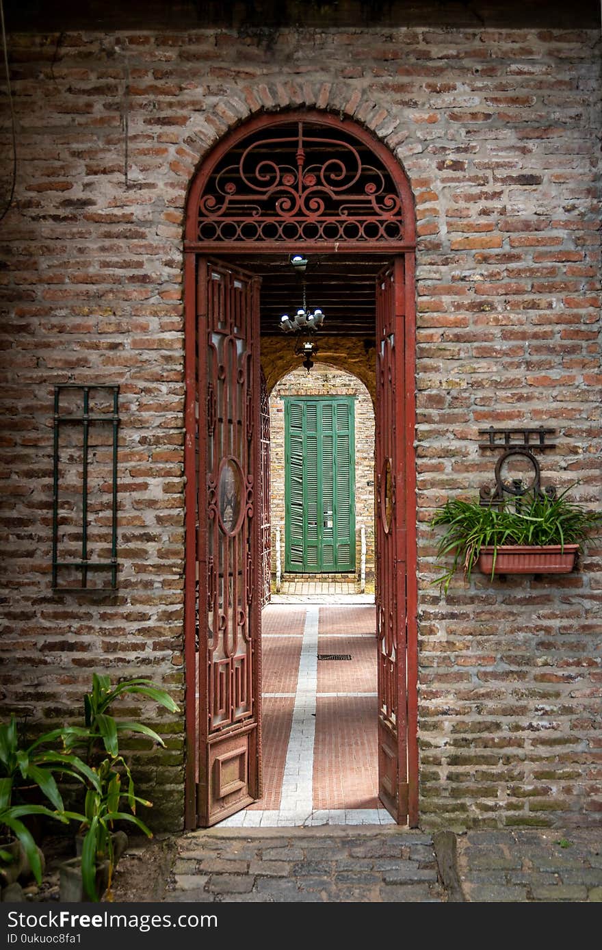 Old brick arch with rusty iron gate open, leading to a passage with a green broken blind at the end of it