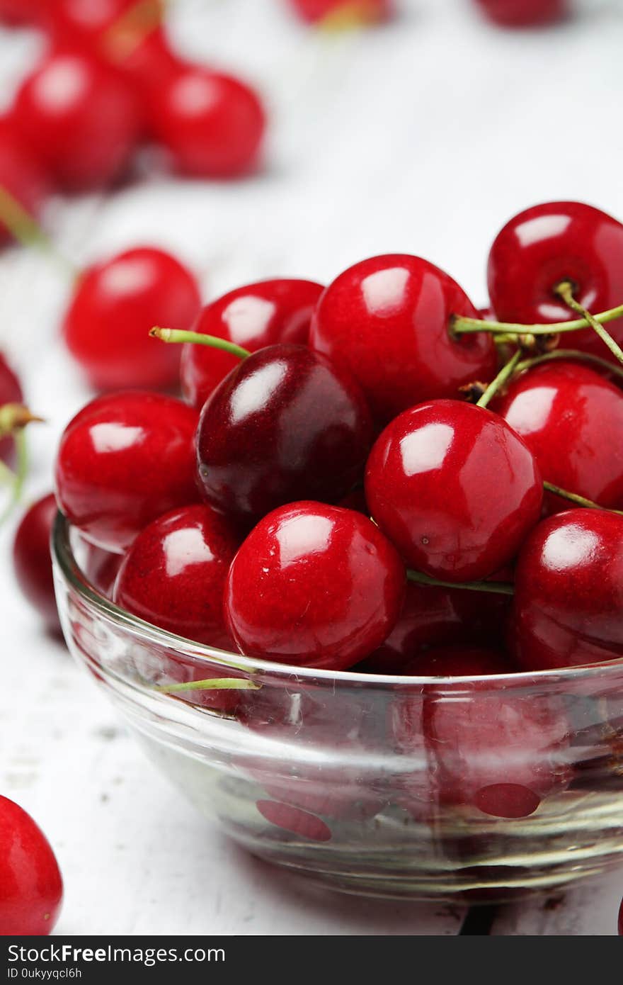 A small glass bowl with ripe fresh cherry on white wooden rustic table