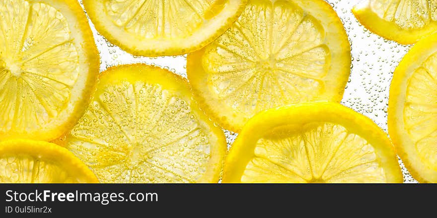 Slices of lemon in water with air bubbles on white background. Close up.