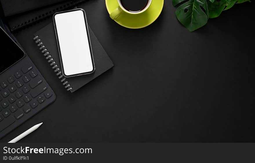 Top view of dark modern workplace with wireless keyboard, mock up smartphone, copy space, office supplies and coffee cup on black table background. Top view of dark modern workplace with wireless keyboard, mock up smartphone, copy space, office supplies and coffee cup on black table background