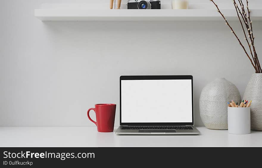 Cropped shot of workplace with blank screen laptop, red coffee cup, decorations on white desk