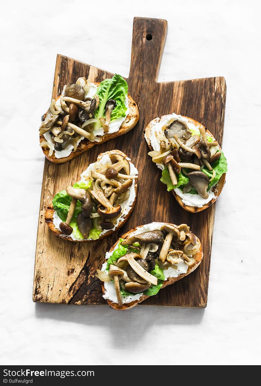 Mixed mushrooms cream cheese green salad on the grill bread sandwiches on a rustic cutting board on a light background, top view