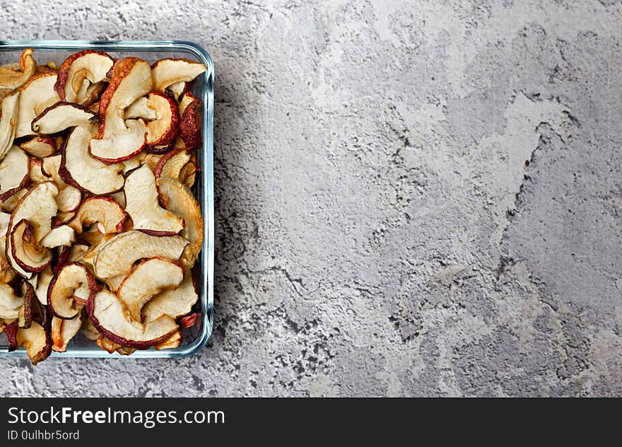 Dried Apple chips in a square glass plate on a gray concrete background. Organic natural food. Top view. Flat lay. Copy space