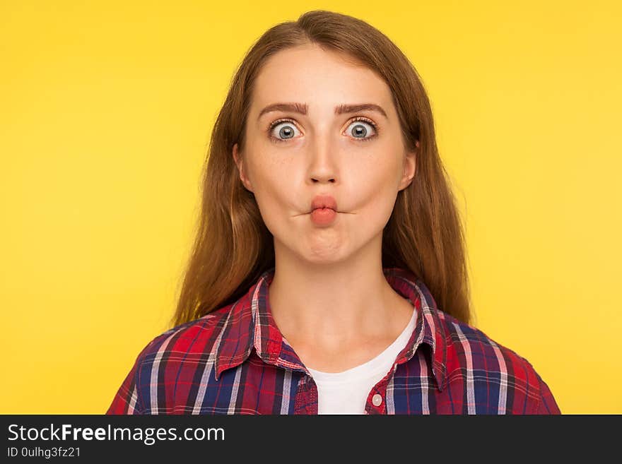 Portrait of amusing funny ginger girl in checkered shirt making fish face and looking with big eyes, confused ridiculous expression, comical wondered grimace. studio shot isolated on yellow background