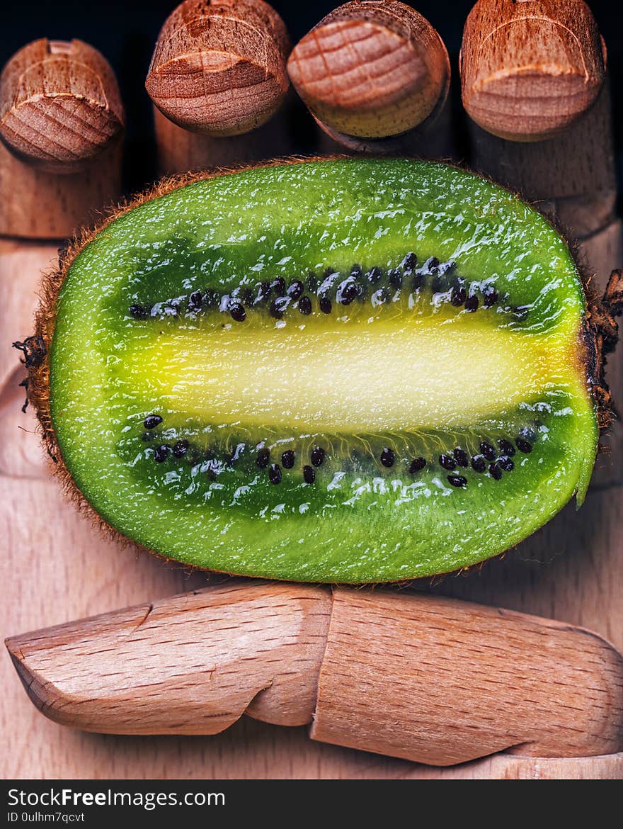 Wooden hand holding a kiwi split in half with black background. Wooden hand holding a kiwi split in half with black background